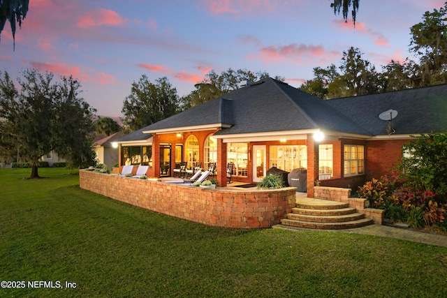 rear view of house featuring a patio, a lawn, and a shingled roof