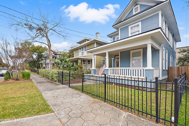 traditional style home featuring a porch, a fenced front yard, and a front lawn