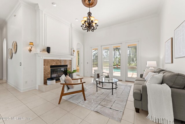 living room with arched walkways, french doors, crown molding, a tiled fireplace, and light tile patterned flooring