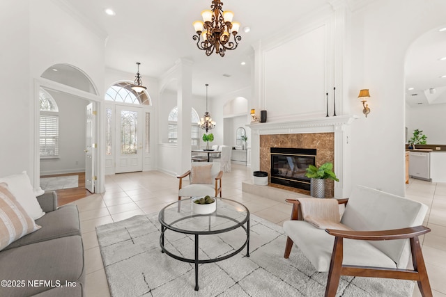 living area featuring arched walkways, light tile patterned floors, a premium fireplace, and a notable chandelier