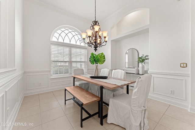 dining room with crown molding, a decorative wall, a notable chandelier, and light tile patterned flooring