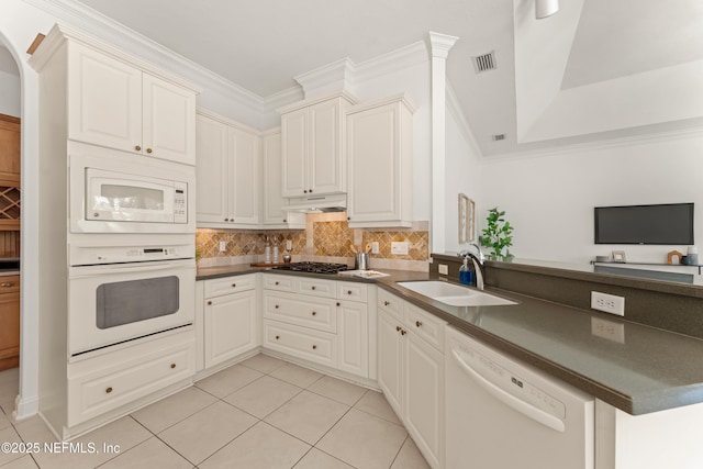 kitchen with white appliances, tasteful backsplash, dark countertops, a peninsula, and a sink