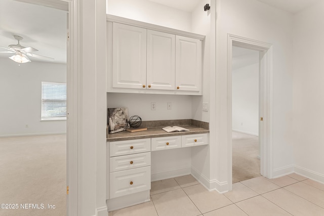 kitchen with light carpet, built in study area, dark countertops, ceiling fan, and white cabinetry