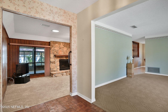 unfurnished living room with a fireplace, visible vents, carpet flooring, a textured ceiling, and baseboards