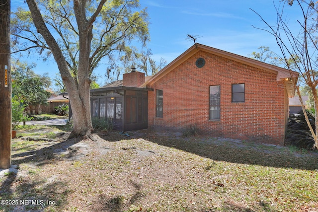 view of property exterior featuring brick siding, a chimney, fence, and a sunroom