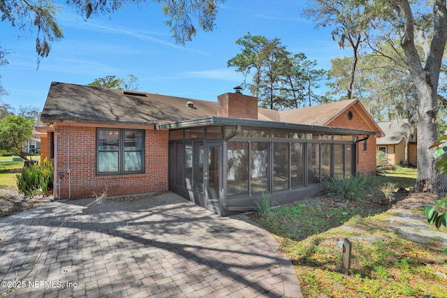 rear view of property with brick siding, a chimney, and a sunroom