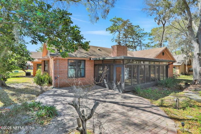 view of front of house featuring a sunroom, a chimney, and brick siding