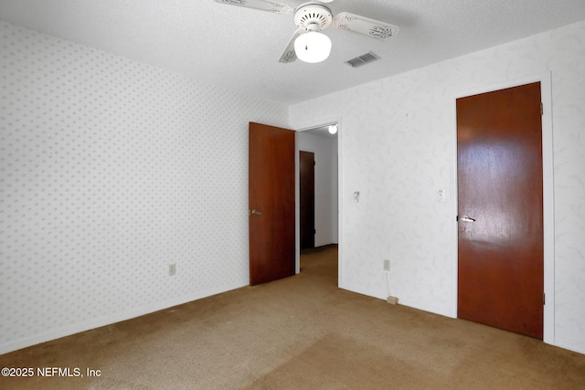 unfurnished bedroom featuring carpet floors, wallpapered walls, visible vents, and a textured ceiling