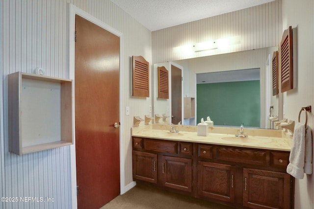 full bathroom with a textured ceiling, double vanity, a sink, and wallpapered walls