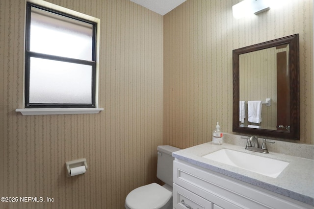 bathroom with toilet, wallpapered walls, and vanity