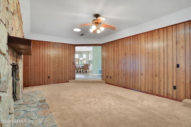 carpeted empty room with a textured ceiling, a ceiling fan, visible vents, and wooden walls