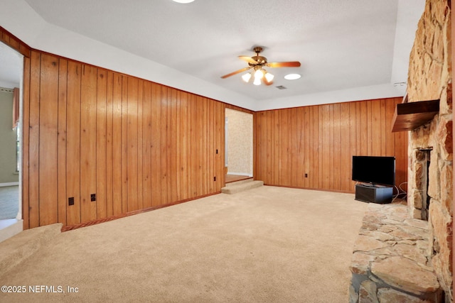 unfurnished living room with carpet flooring, wood walls, a fireplace, and ceiling fan