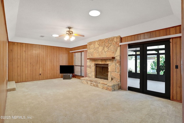 unfurnished living room with carpet floors, french doors, a fireplace, a ceiling fan, and wooden walls