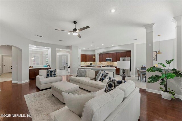 living room with a ceiling fan, arched walkways, dark wood-style flooring, and visible vents