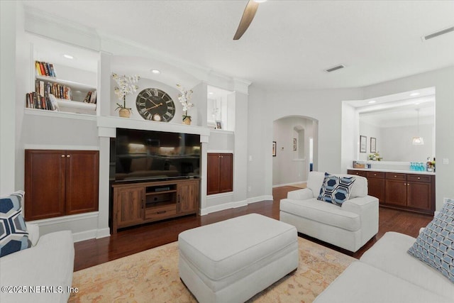 living room featuring built in features, arched walkways, and wood finished floors