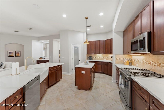 kitchen featuring stainless steel appliances, a kitchen island, a sink, light countertops, and decorative light fixtures