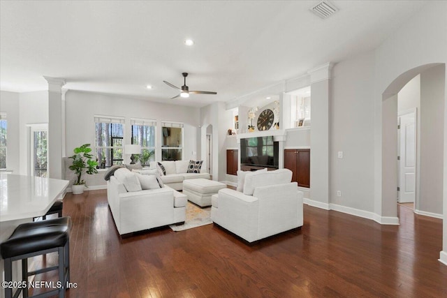 living room with visible vents, arched walkways, dark wood-type flooring, and a glass covered fireplace