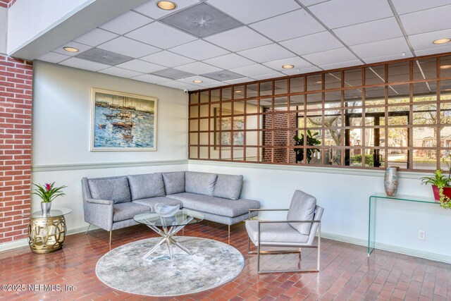 living room with brick floor, a drop ceiling, baseboards, and recessed lighting