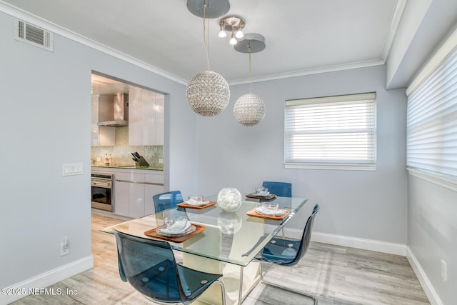 dining room featuring baseboards, light wood-style floors, visible vents, and ornamental molding
