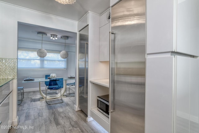 kitchen featuring wood finished floors, hanging light fixtures, white cabinets, appliances with stainless steel finishes, and modern cabinets