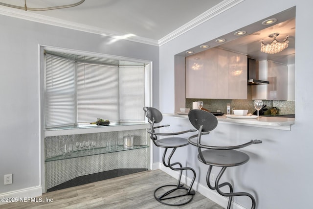 kitchen featuring a kitchen bar, ornamental molding, wood finished floors, wall chimney range hood, and decorative backsplash