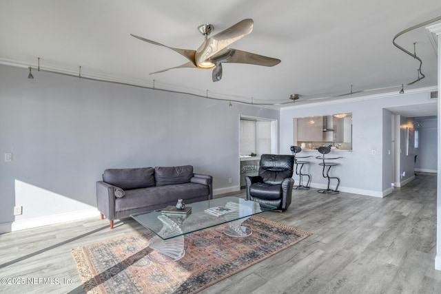 living room with baseboards, crown molding, a ceiling fan, and wood finished floors