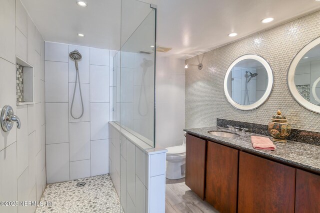 bathroom featuring toilet, tasteful backsplash, tile walls, tiled shower, and vanity