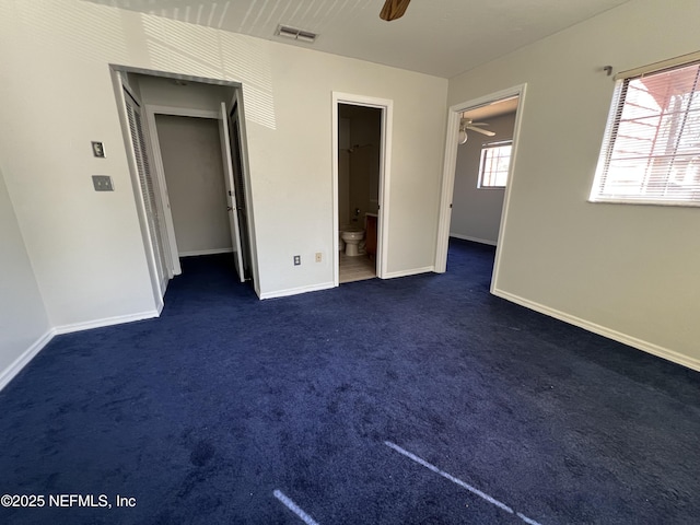 unfurnished bedroom featuring a walk in closet, baseboards, visible vents, and dark colored carpet