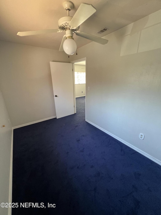 spare room featuring a ceiling fan, dark carpet, visible vents, and baseboards