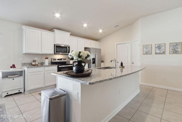 kitchen with light tile patterned floors, appliances with stainless steel finishes, white cabinets, a sink, and an island with sink