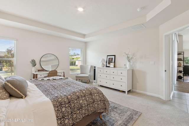 bedroom featuring light carpet, baseboards, visible vents, and a tray ceiling