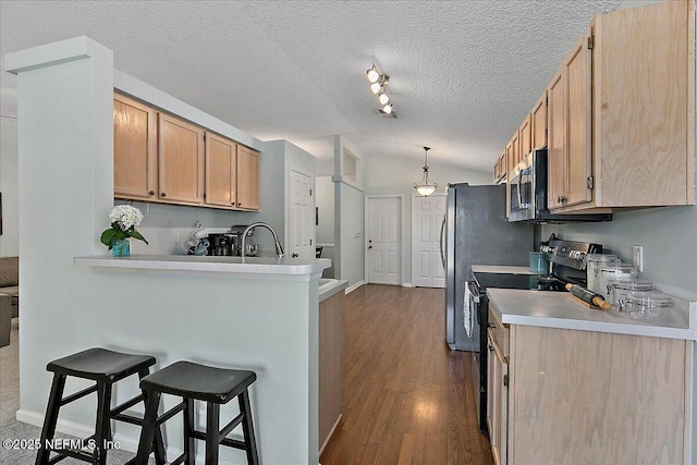 kitchen with dark wood finished floors, appliances with stainless steel finishes, a breakfast bar, a peninsula, and vaulted ceiling