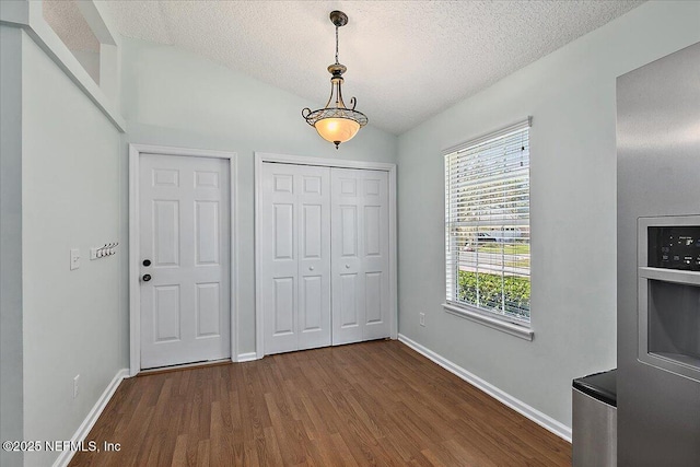 unfurnished bedroom with vaulted ceiling, dark wood-style flooring, a textured ceiling, and baseboards