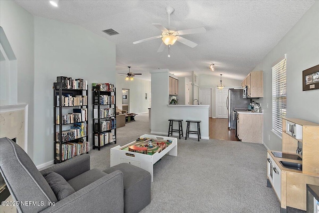 living room with carpet, visible vents, vaulted ceiling, a textured ceiling, and ceiling fan