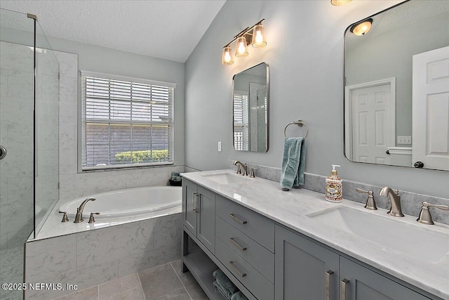 full bath with a textured ceiling, double vanity, a sink, and a garden tub