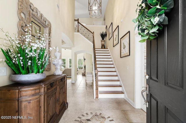 entryway with arched walkways, light tile patterned flooring, a towering ceiling, baseboards, and stairs