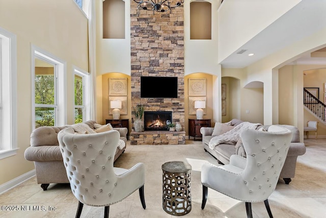 living area with stairs, a stone fireplace, arched walkways, and baseboards