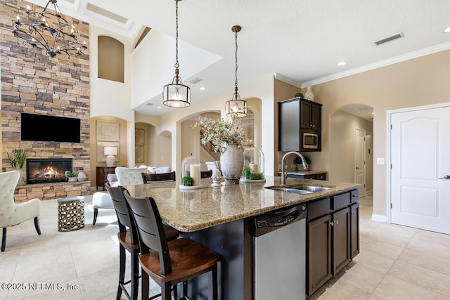 kitchen with light stone counters, a fireplace, a sink, appliances with stainless steel finishes, and a center island with sink