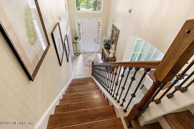 stairs with a high ceiling, wood finished floors, visible vents, and baseboards