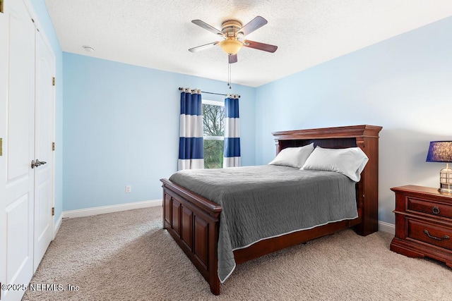 bedroom with light carpet, a textured ceiling, a ceiling fan, and baseboards