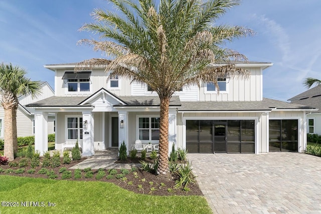 view of front of house with a shingled roof, an attached garage, decorative driveway, a porch, and board and batten siding