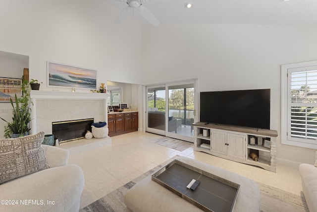 living room featuring light tile patterned floors, baseboards, a ceiling fan, a tiled fireplace, and a high ceiling