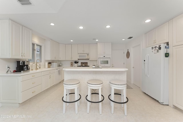 kitchen featuring a breakfast bar area, white appliances, visible vents, light countertops, and an island with sink