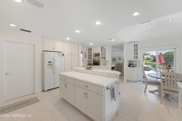 kitchen with visible vents, white cabinets, a kitchen island, glass insert cabinets, and white fridge with ice dispenser