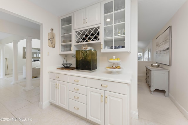 bar featuring light tile patterned floors, decorative columns, and baseboards