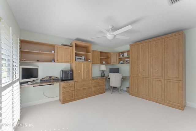 office area featuring light colored carpet, built in study area, ceiling fan, and baseboards