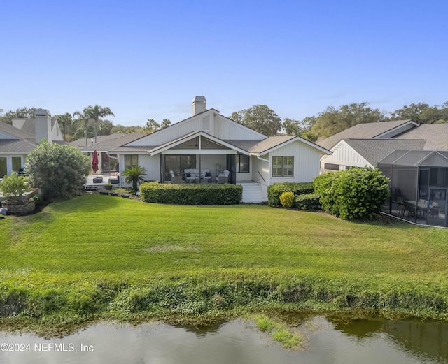 back of property with a lawn, a chimney, and a water view