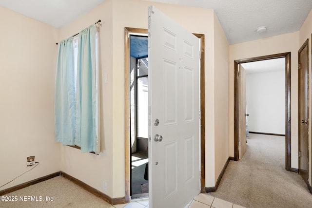 hall featuring a textured ceiling, light colored carpet, and baseboards