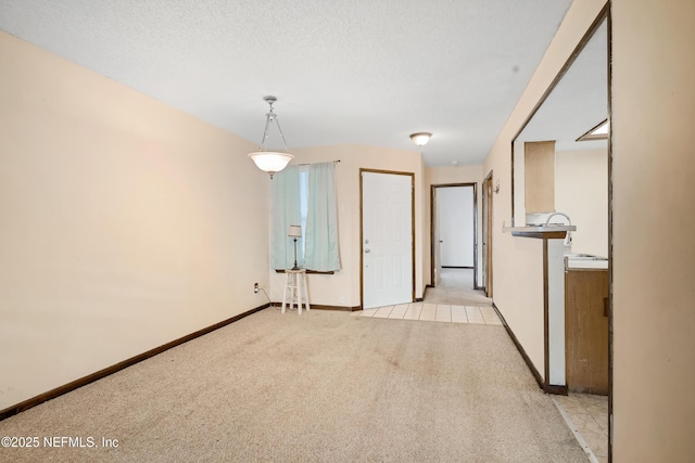 empty room featuring light carpet, a textured ceiling, and baseboards