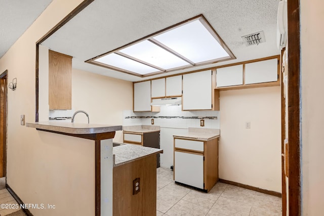 kitchen with a skylight, visible vents, a peninsula, under cabinet range hood, and backsplash